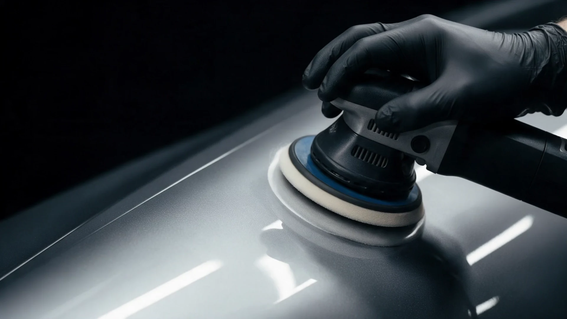 A black-gloved detailer refining silver paint with a polishing pad